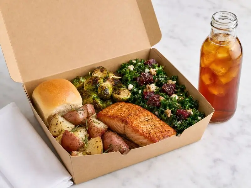 Individually packed meal with baked salmon, rustic potatoes, charred Brussels sprouts, kale salad, and fresh bread — boxed lunch catering for UC Santa Cruz meetings and Watsonville crews